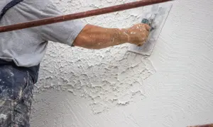 Mano di un operaio che applica la finitura intonaco rustico con una spatola, creando una texture irregolare e caratteristica.