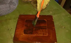 Guanto giallo applica liquido con pennello su un mobile in legno intarsiato. Inizia il processo per come sverniciare un mobile.