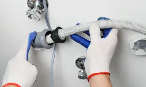Mani guantate collegano il tubo di scarico della lavastoviglie a un raccordo del lavandino.