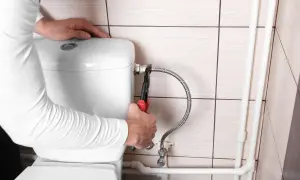 Mani con pinza che lavorano sul tubo flessibile per chiudere acqua cassetta wc.