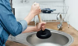 Mani che usano uno sturalavandini per sturare il lavandino intasato in cucina.