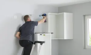 Uomo su scala avvita staffe per come appendere i pensili della cucina. Livella a bolla posizionata.