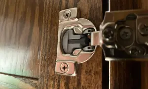 Dettaglio di una cerniera ammortizzata per ante cucina in legno scuro, con viti a vista.