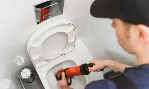 Un idraulico usa uno sturalavandini per liberare un WC. Un filo d'acqua scende nel water, pronto per essere liberato.