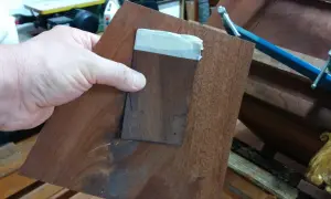 Mano che tiene un pezzo di impiallacciatura di legno scuro, pronto per restaurare un mobile impiallacciato.