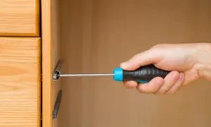 Mano con cacciavite che lavora su guide per cassetti in legno.