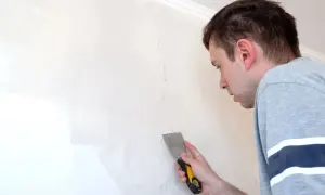 Uomo con spatola ripara una crepa su un muro scrostato, pronto a stuccare.
