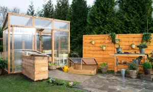 Un giardino con una serra in legno e policarbonato, un banco da lavoro e un'aiuola rialzata. Ideale per chi vuole imparare come costruire una serra.