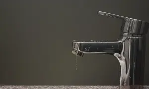 Rubinetto che perde, gocce d'acqua scivolano sul metallo lucido.
