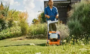 Uomo con tosaerba elettrico in un giardino rigoglioso. Il sole splende, un momento ideale per prendersi cura del prato, ma quando innaffiare il prato?