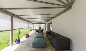 Telo per pergolato fissato con sistema a scomparsa, creando un'area relax con divano e tavola da pranzo.