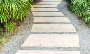 Un sentiero sinuoso in lastre di pietra su ghiaia, un'idea per come pavimentare un giardino senza cemento, circondato da vegetazione lussureggiante.