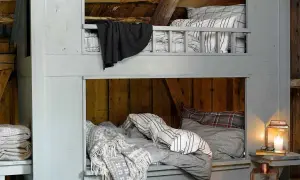 Accogliente letto a castello fai da te in legno grezzo, con coperte a quadri e a righe, perfetto per un rifugio rustico.