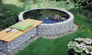 Un incantevole laghetto fuori terra fai da te, circondato da pietre bianche e con una panchina in legno per rilassarsi.
