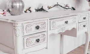 Un tavolo da toeletta bianco, con dettagli intagliati e un effetto invecchiato, pronto per essere restaurato in stile shabby.