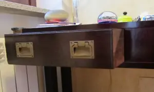 Cassetti che non scorrono, con maniglie dorate su un mobile scuro. Sul piano, oggetti decorativi e libri.