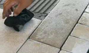 Mano che pulisce le fughe tra le piastrelle bagnate, evidenziando possibili errori posa piastrelle.