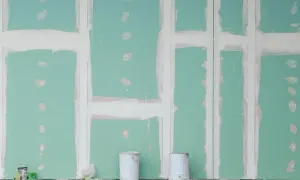 Parete in cartongesso verde con stuccatura delle giunture. Due secchi bianchi in primo piano, detriti sul pavimento. Le misure lastre cartongesso sono fondamentali per questo lavoro.