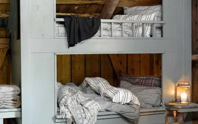 Accogliente letto a castello fai da te in legno grezzo, con coperte a quadri e a righe, perfetto per un rifugio rustico.