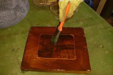 Guanto giallo applica liquido con pennello su un mobile in legno intarsiato. Inizia il processo per come sverniciare un mobile.
