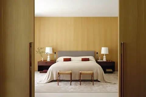 Camera da letto con letto centrale, testiera grigia, comodini in legno scuro e due sgabelli. Ottima idea su come posizionare il letto in camera per un look armonioso.