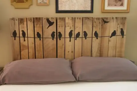 Testiera letto fai da te in legno di pallet con sagome di uccelli su un filo. Un progetto creativo per la tua camera da letto.