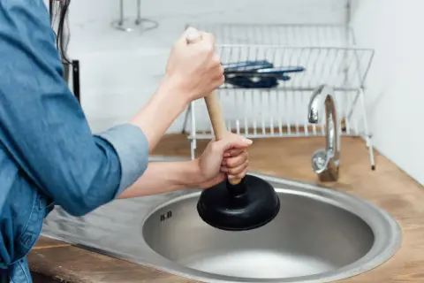Mani che usano uno sturalavandini per sturare il lavandino intasato in cucina.