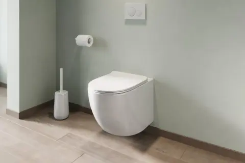 Un moderno bagno con montaggio sanitari sospesi: water a parete, scopino bianco e rotolo di carta igienica su parete verde pastello.