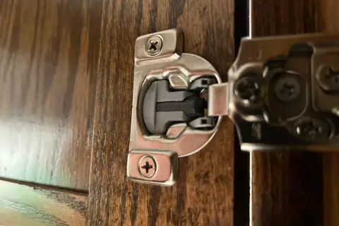 Dettaglio di una cerniera ammortizzata per ante cucina in legno scuro, con viti a vista.