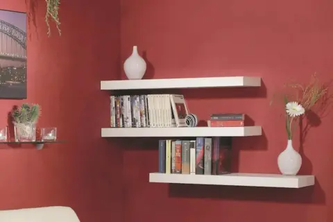 Mensole bianche a muro con libri, vasi e una pianta. Una guida visiva su come montare una mensola.