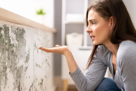 Donna preoccupata osserva muffa su muro. Scopri come togliere umidità in casa per un ambiente più sano.