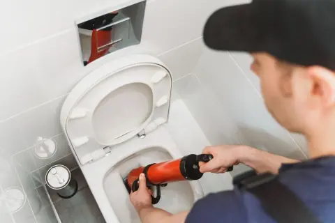 Un idraulico usa uno sturalavandini per liberare un WC. Un filo d'acqua scende nel water, pronto per essere liberato.