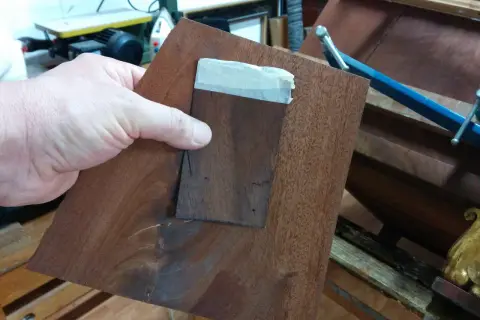 Mano che tiene un pezzo di impiallacciatura di legno scuro, pronto per restaurare un mobile impiallacciato.