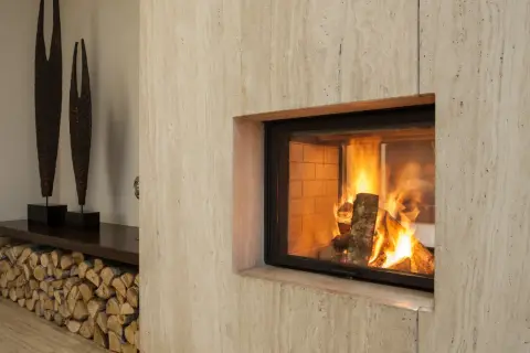 Un camino moderno con fiamme vive, pronto per lo spazzacamino. Legna accatastata e sculture decorative completano l'arredo.