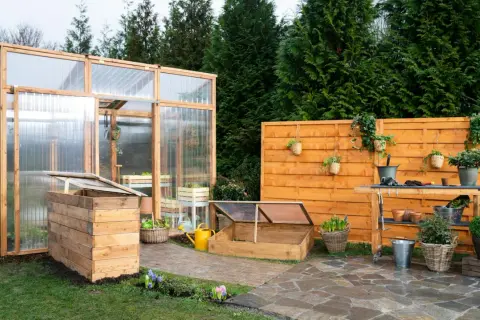 Un giardino con una serra in legno e policarbonato, un banco da lavoro e un'aiuola rialzata. Ideale per chi vuole imparare come costruire una serra.