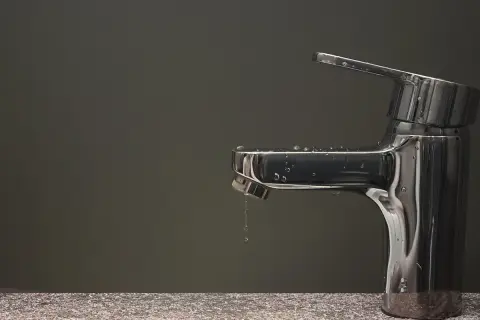 Rubinetto che perde, gocce d'acqua scivolano sul metallo lucido.