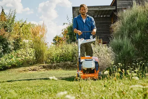 Uomo con tosaerba elettrico in un giardino rigoglioso. Il sole splende, un momento ideale per prendersi cura del prato, ma quando innaffiare il prato?