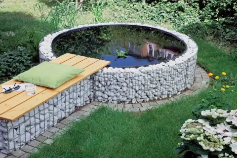 Un incantevole laghetto fuori terra fai da te, circondato da pietre bianche e con una panchina in legno per rilassarsi.