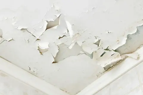 Soffitto scrostato e macchiato, segnale evidente di come riconoscere le infiltrazioni d'acqua. La pittura si stacca a chiazze, rivelando l'umidità sottostante.