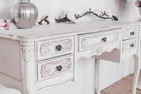 Un tavolo da toeletta bianco, con dettagli intagliati e un effetto invecchiato, pronto per essere restaurato in stile shabby.