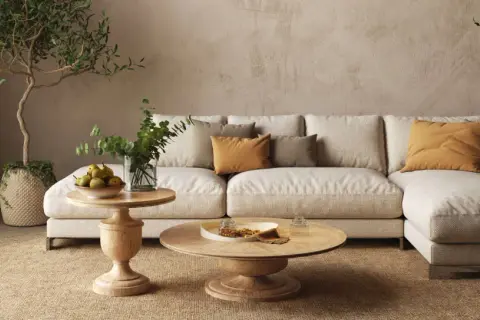 Un divano componibile beige, tavolini in legno, piante e cuscini color ocra creano salotti caldi e accoglienti, perfetti per rilassarsi.