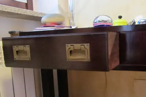 Cassetti che non scorrono, con maniglie dorate su un mobile scuro. Sul piano, oggetti decorativi e libri.