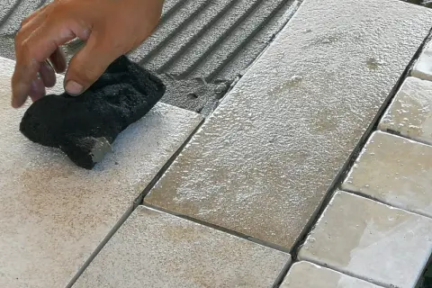 Mano che pulisce le fughe tra le piastrelle bagnate, evidenziando possibili errori posa piastrelle.
