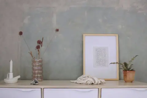 Parete con effetto materico, ideale per chi vuole imparare come pitturare una parete con stile. Arredamento minimalista con vasi, candela e quadro.