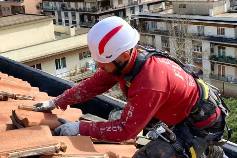Operaio con imbracatura lavora sul tetto per isolare tetto senza togliere tegole, applicando materiale isolante.