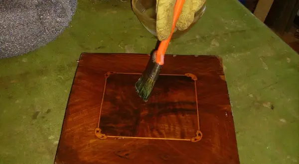 Guanto giallo applica liquido con pennello su un mobile in legno intarsiato. Inizia il processo per come sverniciare un mobile.