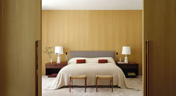 Camera da letto con letto centrale, testiera grigia, comodini in legno scuro e due sgabelli. Ottima idea su come posizionare il letto in camera per un look armonioso.