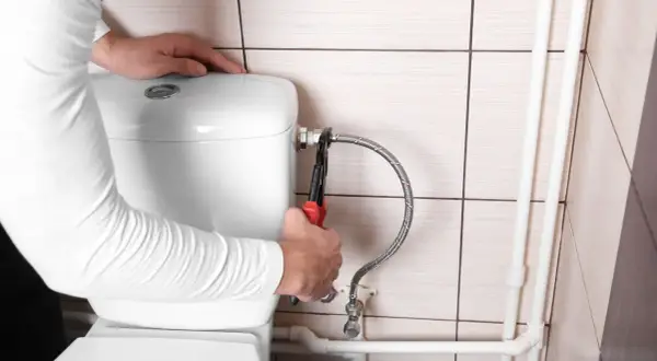 Mani con pinza che lavorano sul tubo flessibile per chiudere acqua cassetta wc.