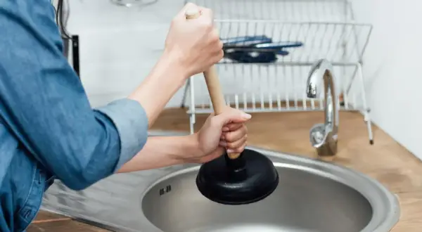 Mani che usano uno sturalavandini per sturare il lavandino intasato in cucina.