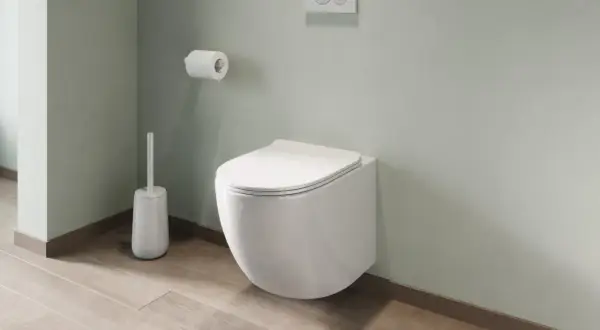 Un moderno bagno con montaggio sanitari sospesi: water a parete, scopino bianco e rotolo di carta igienica su parete verde pastello.